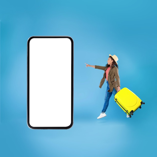 Signora turistica nera che salta vicino all'enorme sfondo blu del telefono cellulare