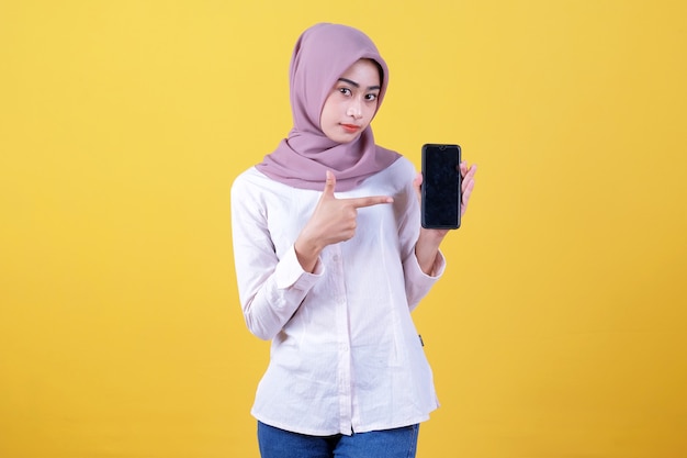 Sii intelligente compra questo dispositivo, ritratto di giovane donna asiatica che ride ad alta voce, indossa l'hijab che punta allo smartphone, mostra lo schermo del dispositivo