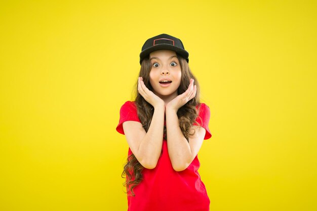 Sii la tua etichetta. ragazza sorpresa in berretto hipster alla moda. bambino hipster su sfondo giallo. infanzia felice. bellezza e moda. piccola ragazza con i capelli lunghi. bella ragazza con lunghi capelli ricci. moda bambino.