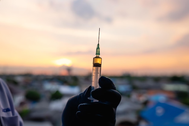 Silhouette della mano del medico in guanti blu che tengono il vaccino contro il coronavirus