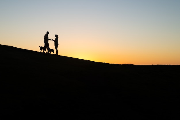 Silhouette di coppia con due cani in una collina al tramonto