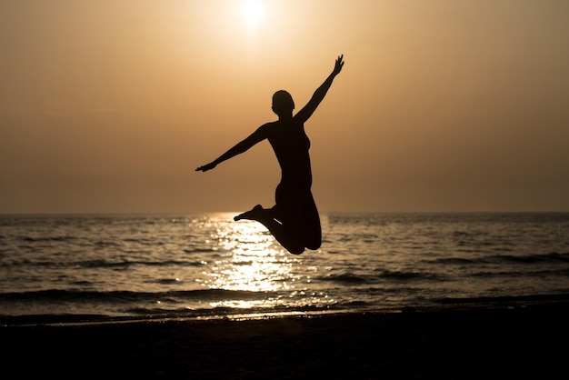 Silhouette di donna con le mani alzate e saltare sulla spiaggia al tramonto Copia spazio testo