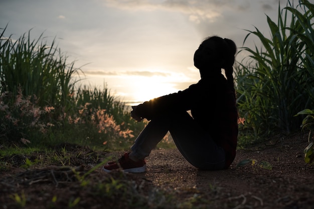 Silhouette di donna contadina seduta nella piantagione di canna da zucchero sullo sfondo la sera del tramonto