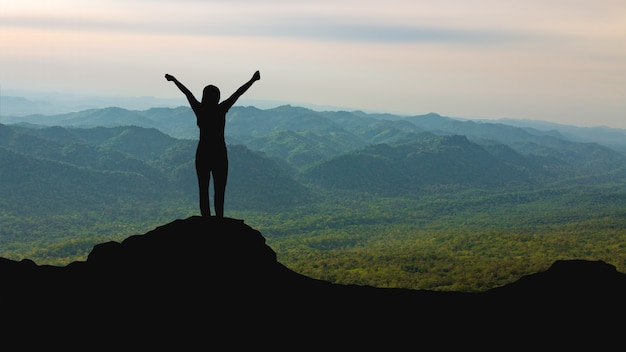 Silhouette di donna sulla cima della montagna sopra il cielo e la luce del sole