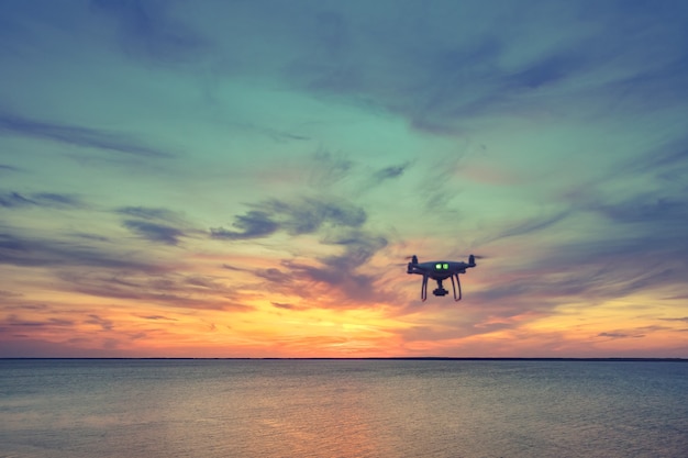 Silhouette di Drone Quad elicottero che vola nel cielo. Vista panoramica aerea del tramonto sull'oceano. Drammatica scena serale pittoresca. Oceano e cielo nuvoloso colorato in background. Paesaggio della natura