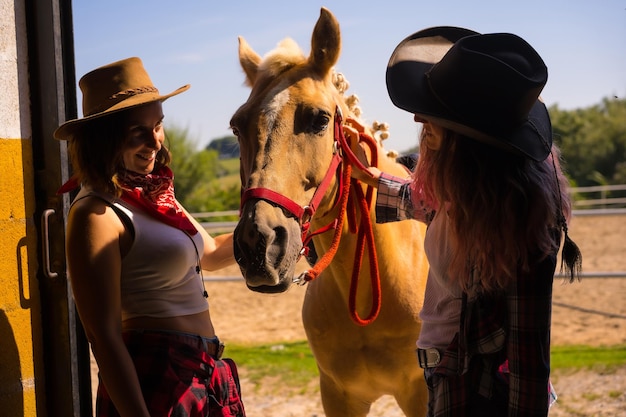 Silhouette di due donne cowgirl che entrano nella stalla con un cavallo da cavallo, con abiti sudamericani