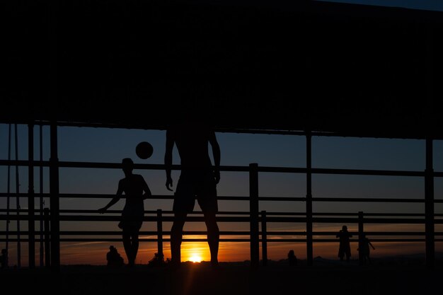 silhouette di due giovani che giocano a calcio su una passerella portuale su una spiaggia in Portogallo al tramonto