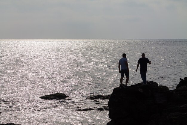 Silhouette di due uomini in piedi su una grande roccia in riva all'oceano. Lanzarote, Spagna.