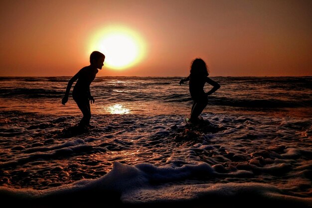 Silhouette di fratelli che giocano in mare contro il cielo durante il tramonto