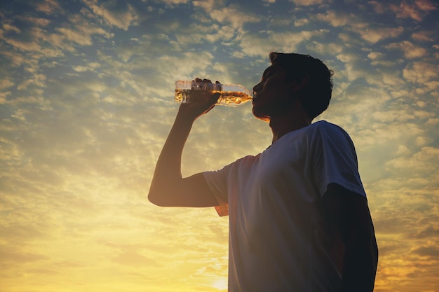 Silhouette di giovane corridore con una bottiglia di acqua fresca dopo l'allenamento all'aperto.