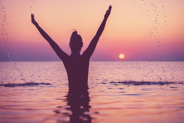 silhouette di giovane donna che pratica yoga sulla spiaggia all'alba