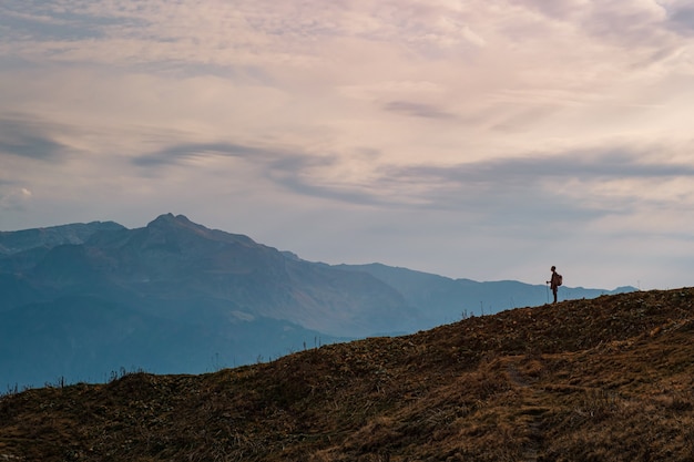 Silhouette di giovane maschio hipster in montagna in autunno. Concetto di destinazione di viaggio di scoperta. Turista sullo sfondo di alte rocce. Sport e concetto di vita attiva.