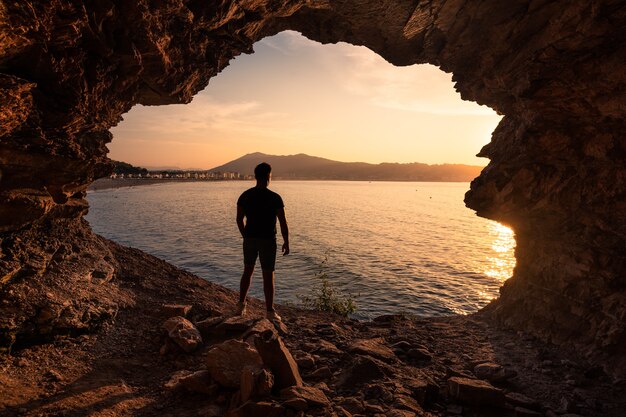 Silhouette di giovane uomo in una grotta costiera vicino alla spiaggia di Hendaia, nei Paesi Baschi.