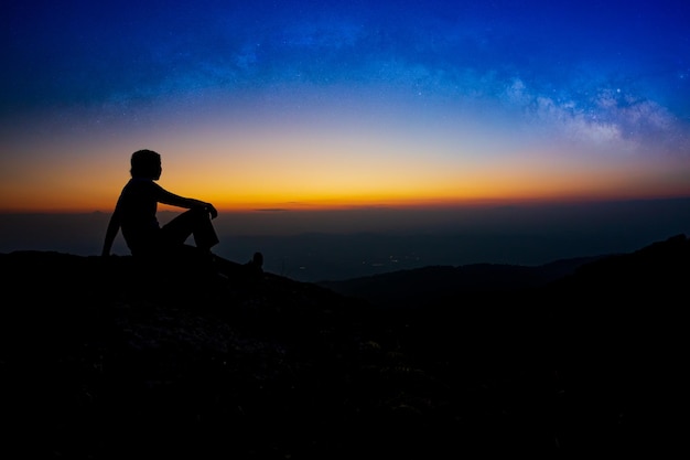 Silhouette di giovane uomo seduto sulla cima della montagna vista da solo durante l'alba Guarda il cielo Vista