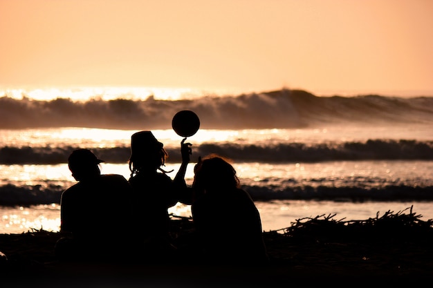 Silhouette di giovani amici che giocano con una palla sulla spiaggia al tramonto