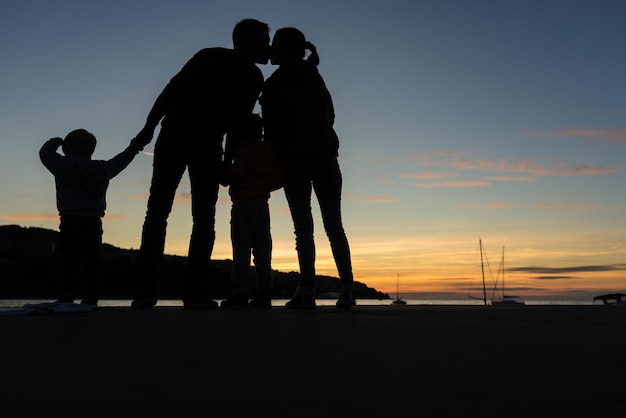 Silhouette di giovani coppie che si baciano mentre stanno in riva al mare di sera