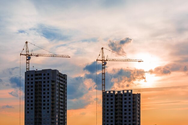 Silhouette di gru a torre e edifici alti multipiano incompiuti in costruzione sotto i raggi del sole al tramonto del bellissimo tramonto