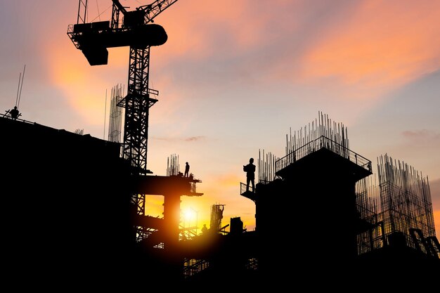 Silhouette di ingegnere e lavoratore che controlla il progetto nel cantiere di fondo del cantiere al tramonto in serata