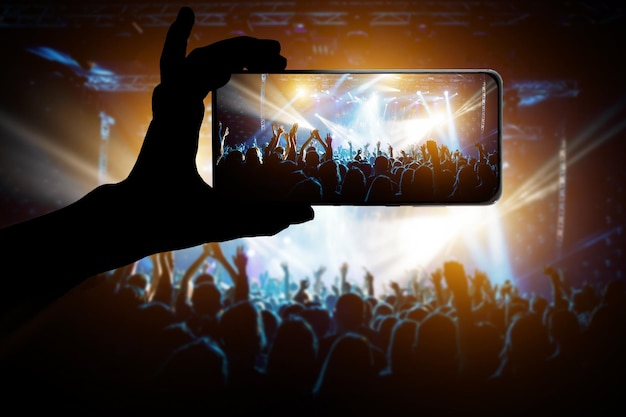 Silhouette di mano utilizzando il telefono con fotocamera per scattare foto e video al festival di concerti pop
