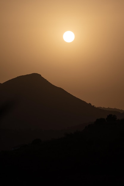 Silhouette di montagne mentre cala il tramonto con il sole sullo sfondo all'ora arancione