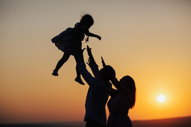 Silhouette di padre e madre che giocano con la figlia del bambino al tramonto