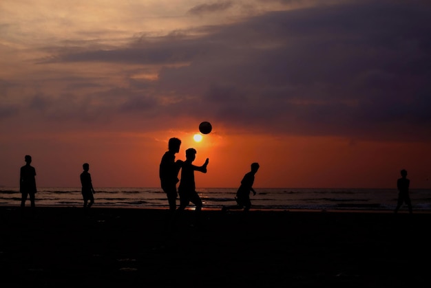 Silhouette di persone che giocano sulla spiaggia contro il cielo durante il tramonto