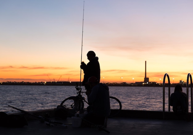 Silhouette di persone che pescano con la mosca sul molo del fiume durante il tramonto
