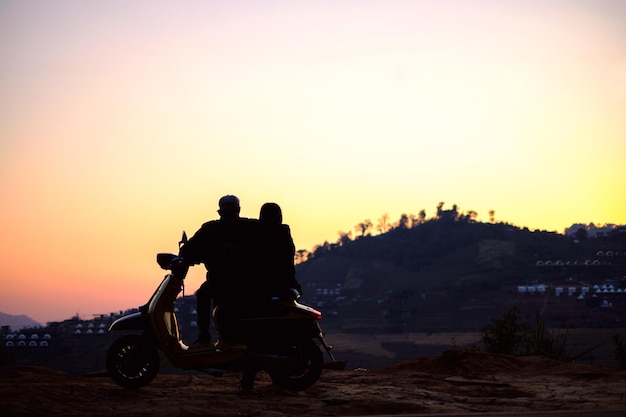 Silhouette di persone sedute su una moto contro il cielo durante il tramonto