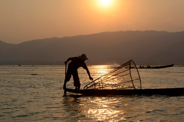 Silhouette di pescatori con la rete da pesca sopra la barca sul lago al tramonto