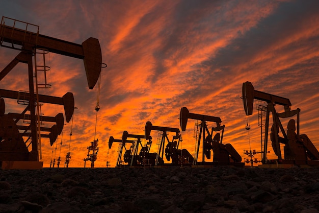 Silhouette di pompe di petrolio sul campo contro un cielo nuvoloso durante il tramonto