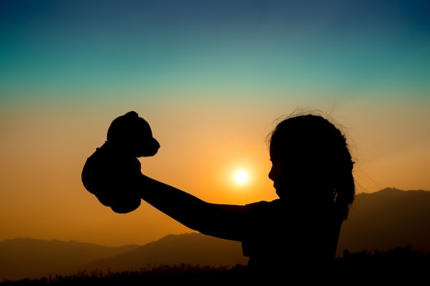 silhouette di ragazza in piedi da solo e mano che tiene orsacchiotto in un momento al tramonto