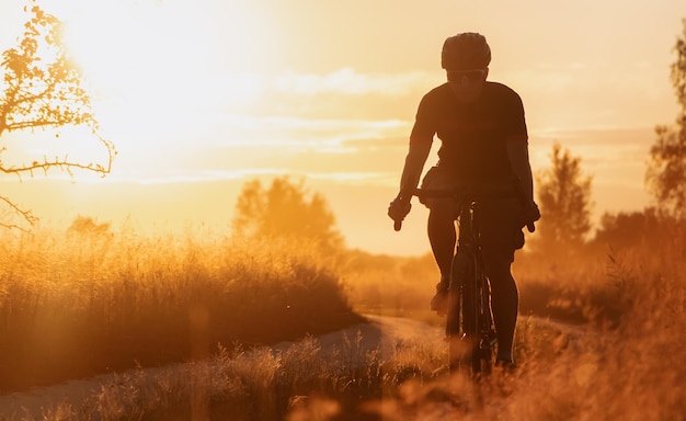 Silhouette di un ciclista su una bici da ghiaia in sella a un sentiero di campagna al tramonto