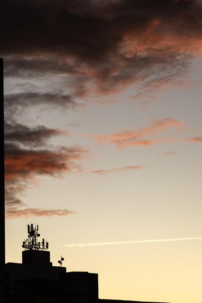 Silhouette di un edificio con antenne di comunicazione contro il tramonto arancione sullo sfondo