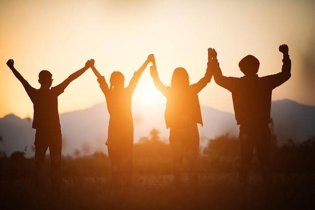 Silhouette di un felice team aziendale umano che fa le mani alte sopra la testa nel cielo al tramonto tempo serale sfondo per il lavoro di squadra aziendale concetto e libertà