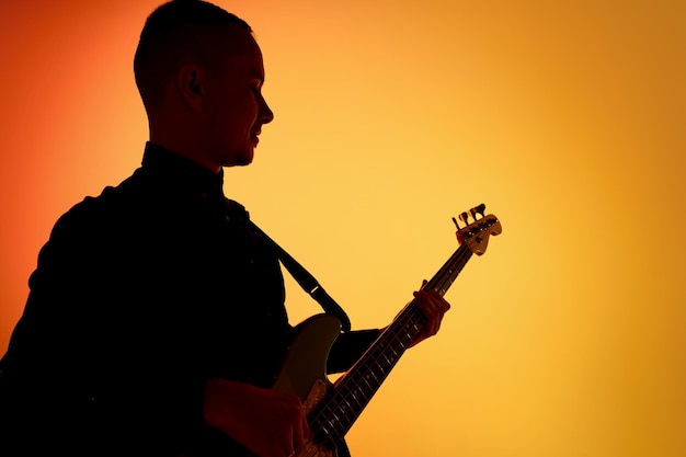 Silhouette di un giovane chitarrista maschio caucasico isolato su uno studio sfumato blu-rosa in luce al neon
