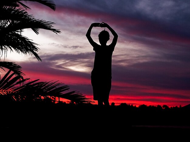 Silhouette di un giovane in piedi con le braccia alzate contro il cielo durante il tramonto