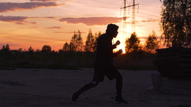 Silhouette di un giovane pugile che si allena per dare dei calci al tramonto al parco cittadino