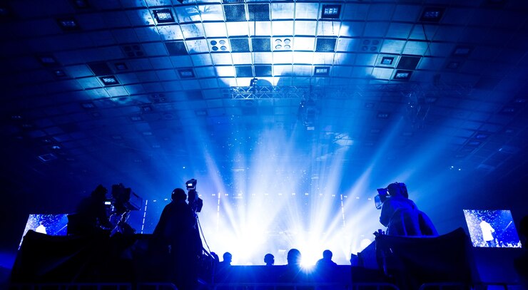 Silhouette di un gruppo di cameraman che trasmettono un evento. I lavoratori sono su un'alta piattaforma sullo sfondo di travi luminose.