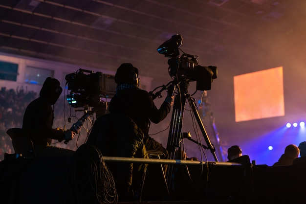 Silhouette di un gruppo di cameramen che trasmettono un evento. I lavoratori sono su una piattaforma alta