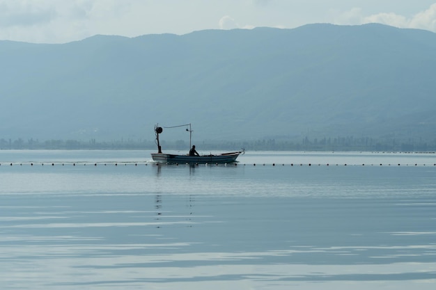 Silhouette di un pescatore su una barca che galleggia su un lago sullo sfondo delle montagne. Tacchino