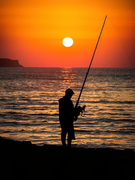 Silhouette di un pescatore sulla costa del mare al tramonto