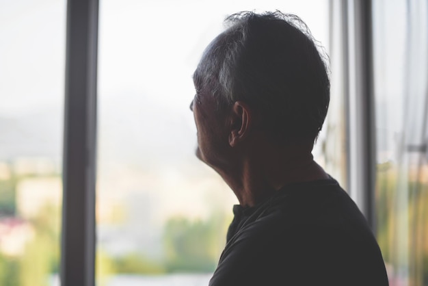 Silhouette di un uomo anziano su uno sfondo di finestra. Vecchiaia. Pensionato di depressione. Solitudine in pensione.