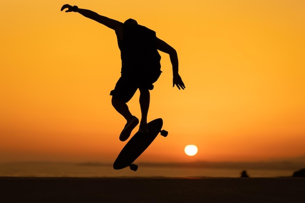 Silhouette di un uomo che esegue un trucco da skateboard al tramonto arancione brillante