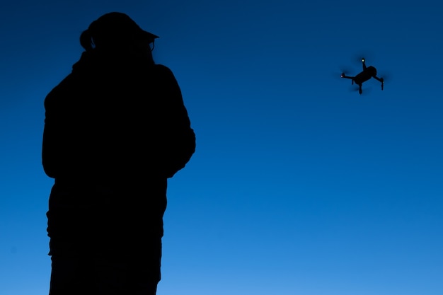 Silhouette di un uomo che fa funzionare un drone in un cielo blu senza nuvole