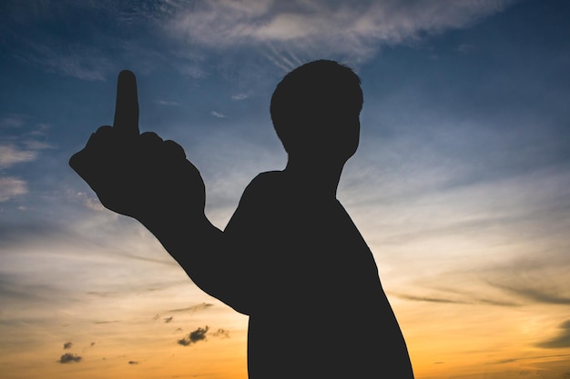 Silhouette di un uomo che mostra un gesto osceno contro il cielo durante il tramonto