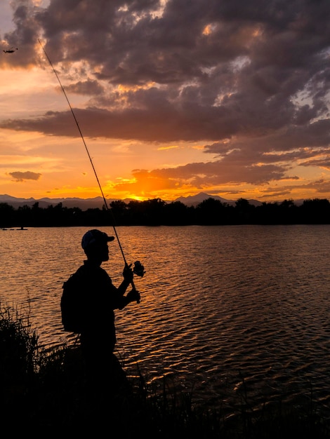 Silhouette di un uomo che pesca in mare contro il cielo durante il tramonto