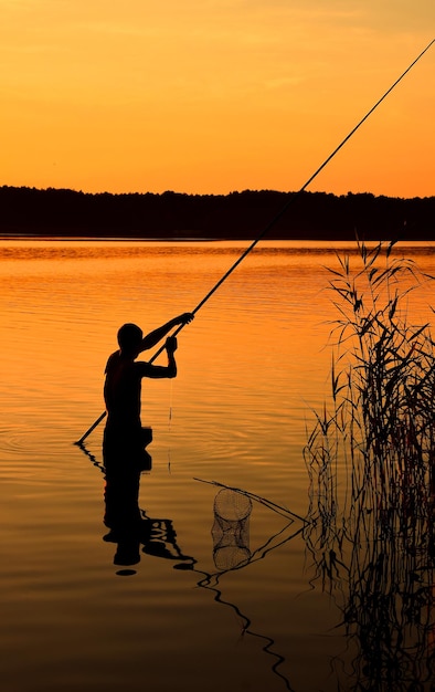 Silhouette di un uomo che pesca sul lago al crepuscolo