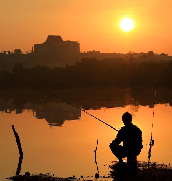 Silhouette di un uomo che pesca sul lago contro un cielo arancione durante il tramonto