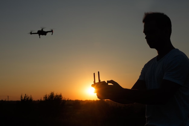 Silhouette di un uomo che pilota un drone in aria con un telecomando nelle sue mani sul pilota al tramonto