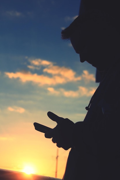 Silhouette di un uomo che usa un telefono cellulare contro il cielo durante il tramonto